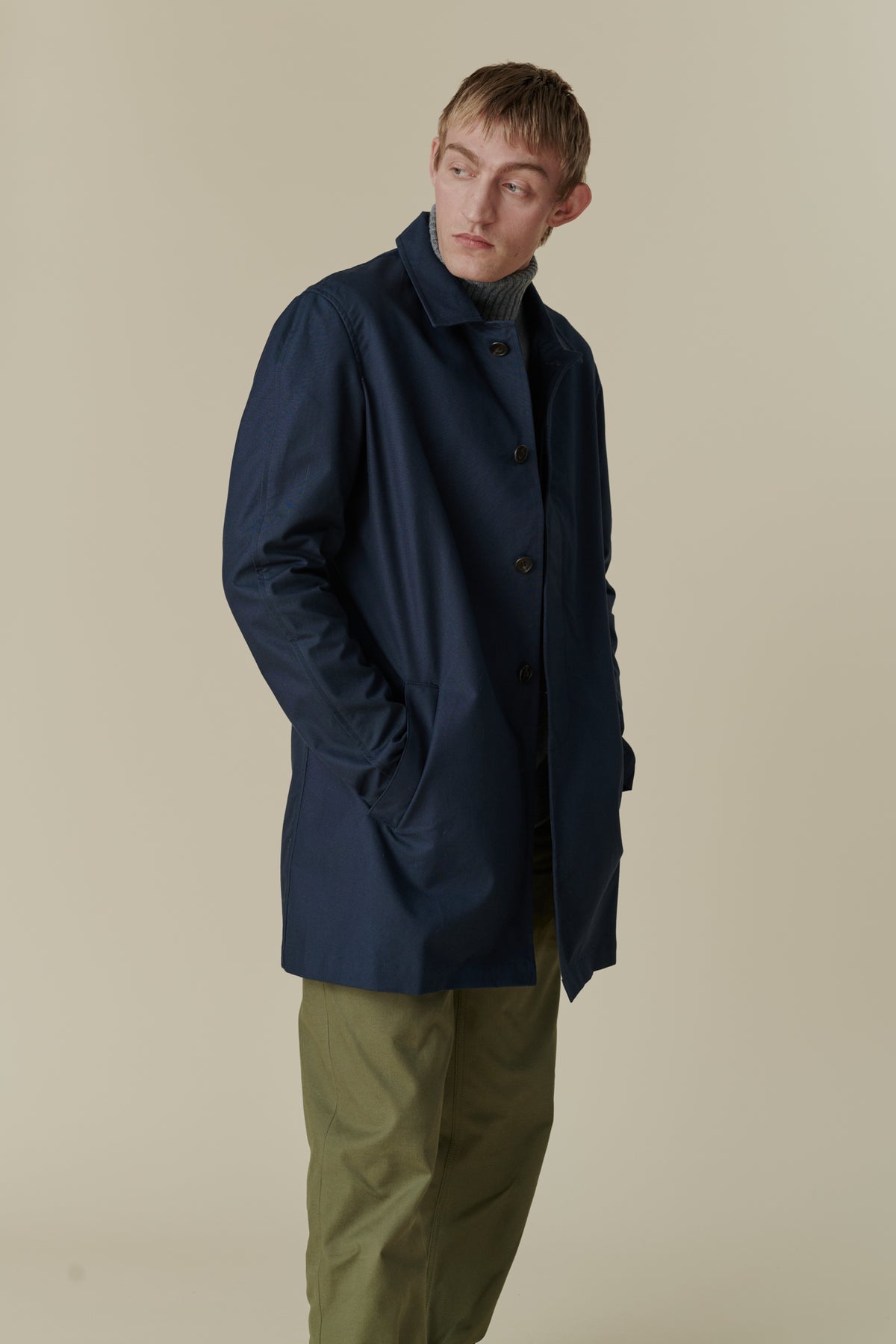 Side angle, knee up image of blonde, white male wearing raincoat in navy