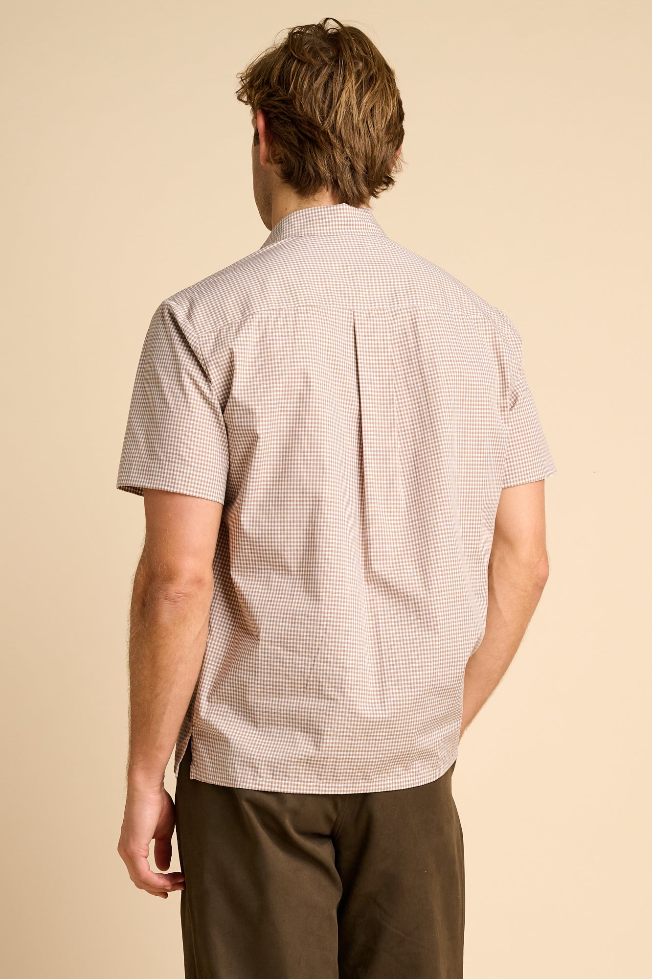 Man wearing a patterned shirt and brown pants on a beige background