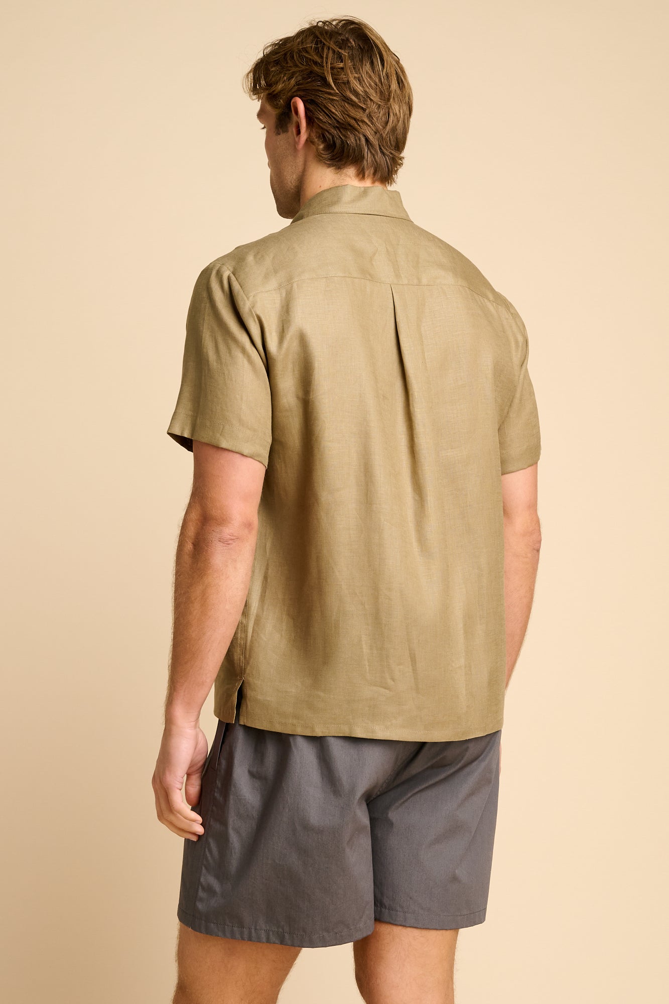 Man wearing a olive short-sleeve shirt and grey shorts on a beige background