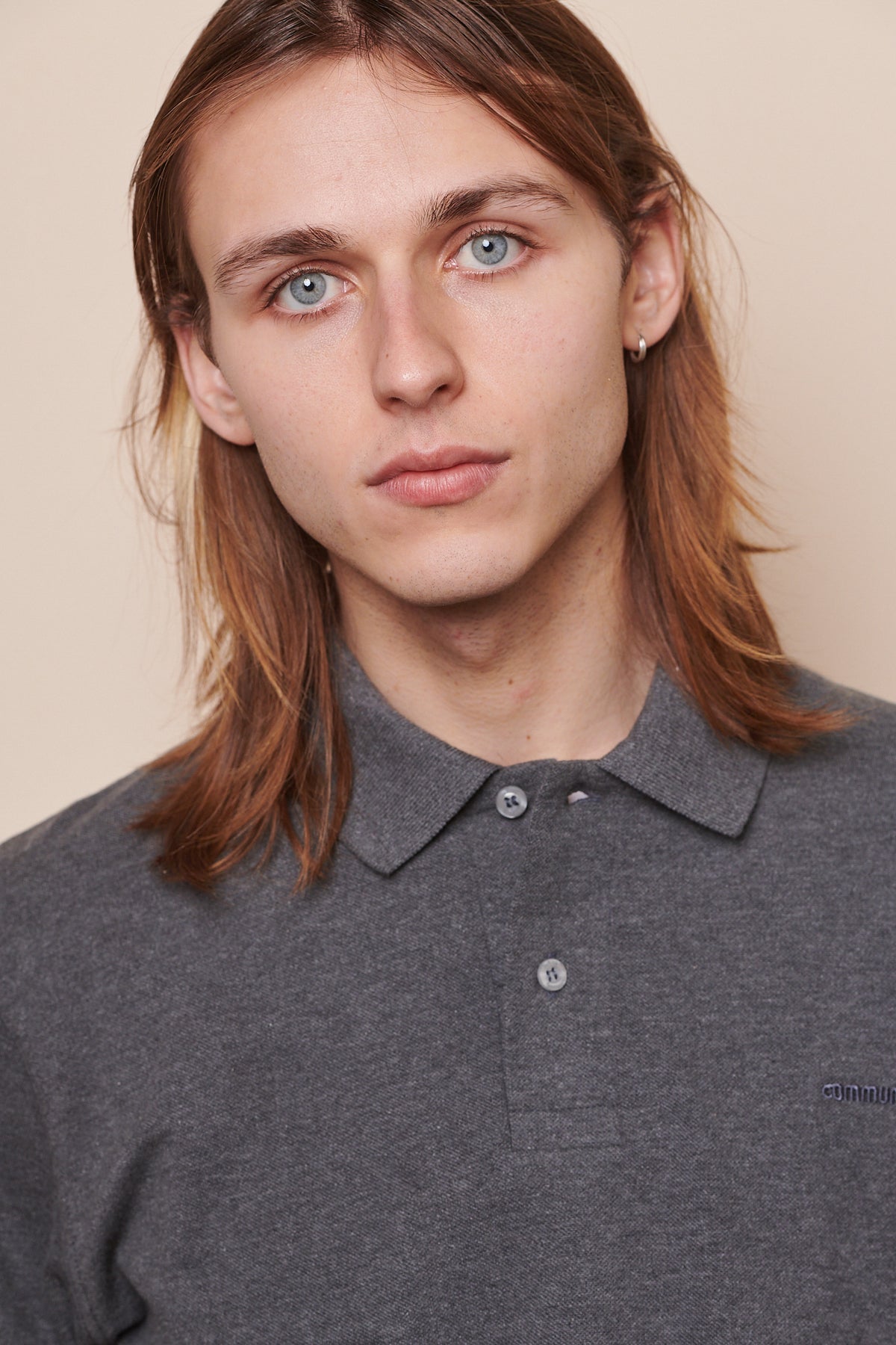 Portrait of male wearing polo shirt in grey marl with top button undone. 'Community' embroidered in matching grey thread on chest