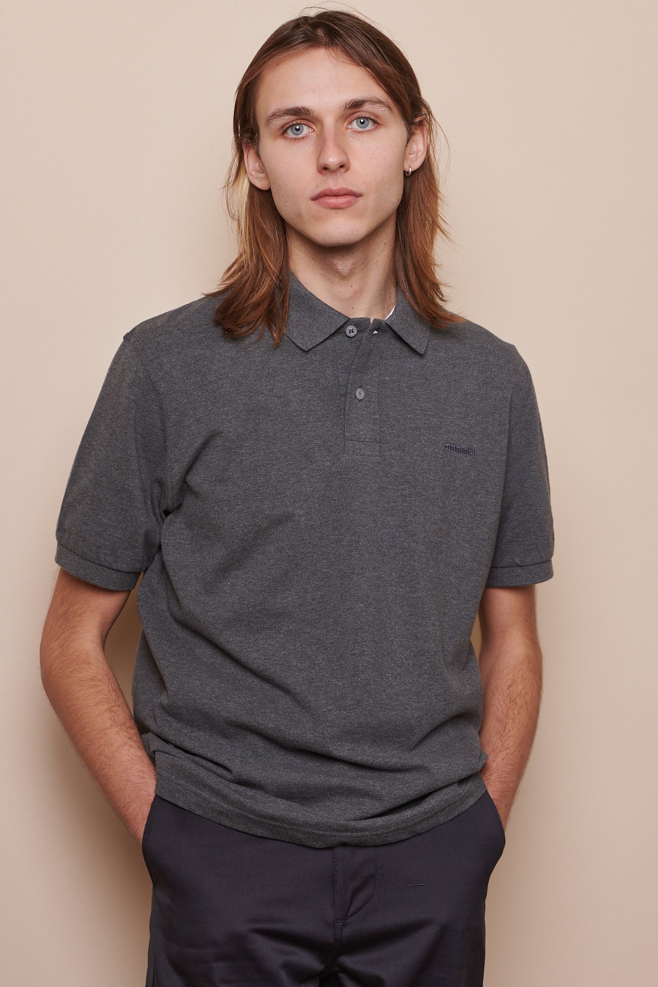 Thigh up image of white male with shoulder length hair wearing short sleeve polo shirt in grey marl