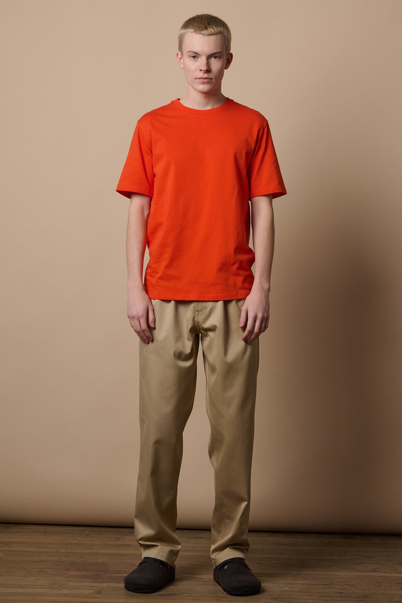Full body image of white male with short blonde hair wearing short sleeve t shirt in flame red