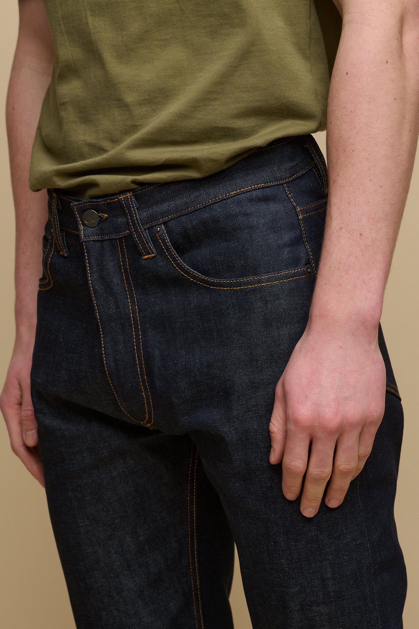 Close up detail shot of the back of men's straight cut selvedge jeans in indigo raw denim with tobacco contrast stitching.  Belt loops and CC logo jeans patch on the back of waistband with two back pockets.