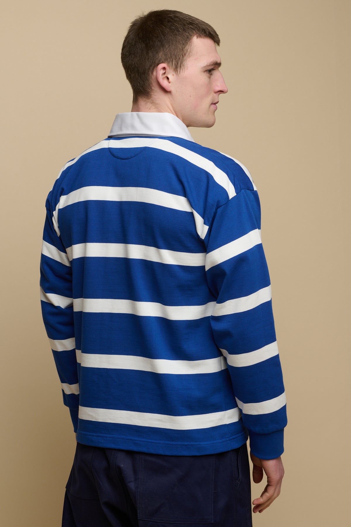 Thigh up image of the back of brunet male wearing stripe rugby shirt in blue and white