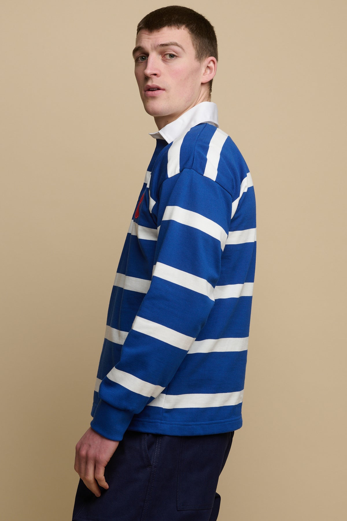 The side of brunet male wearing blue and white stripe logo rugby shirt