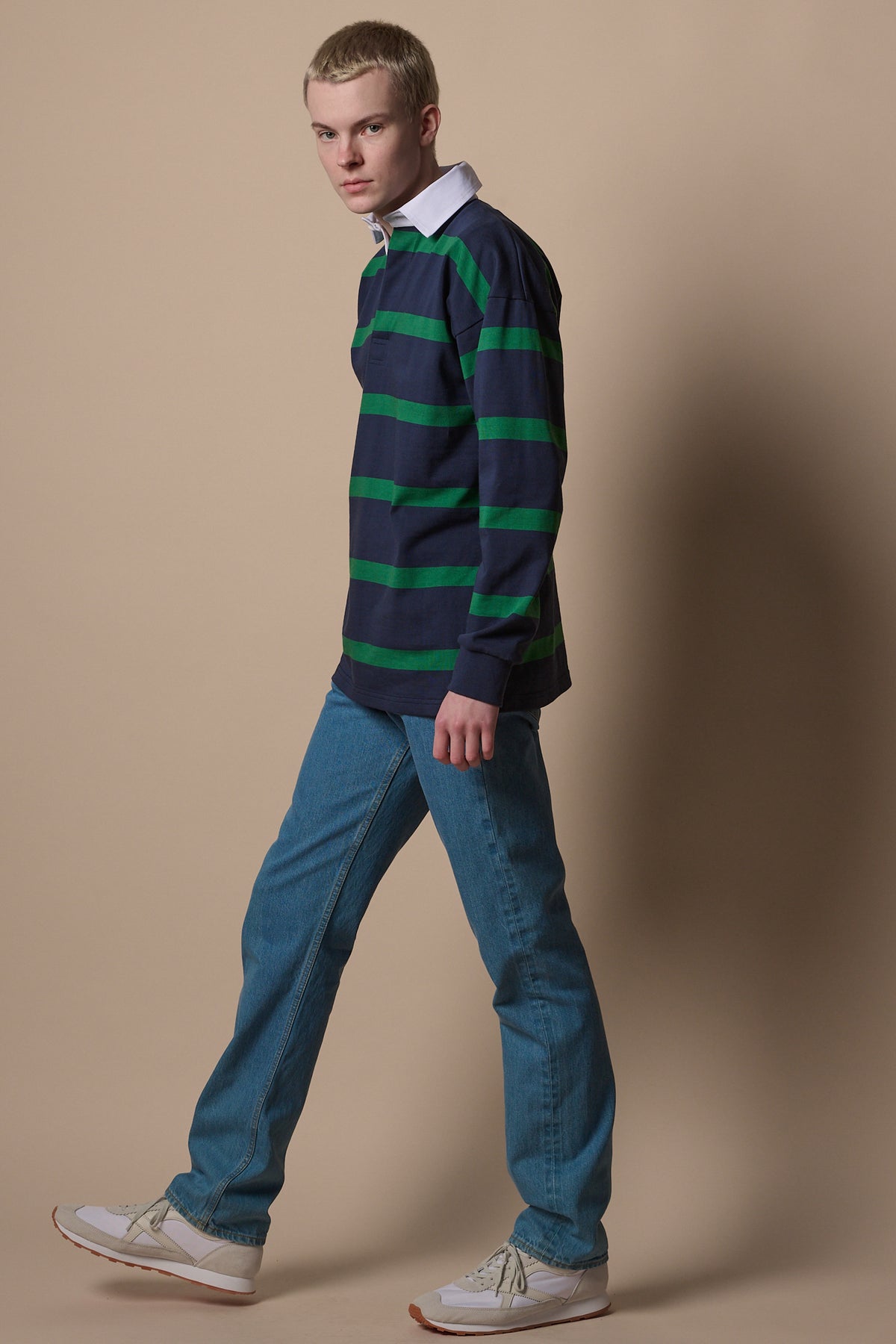 blonde male wearing stripe rugby shirt in navy emerald worn with blue jeans. 
