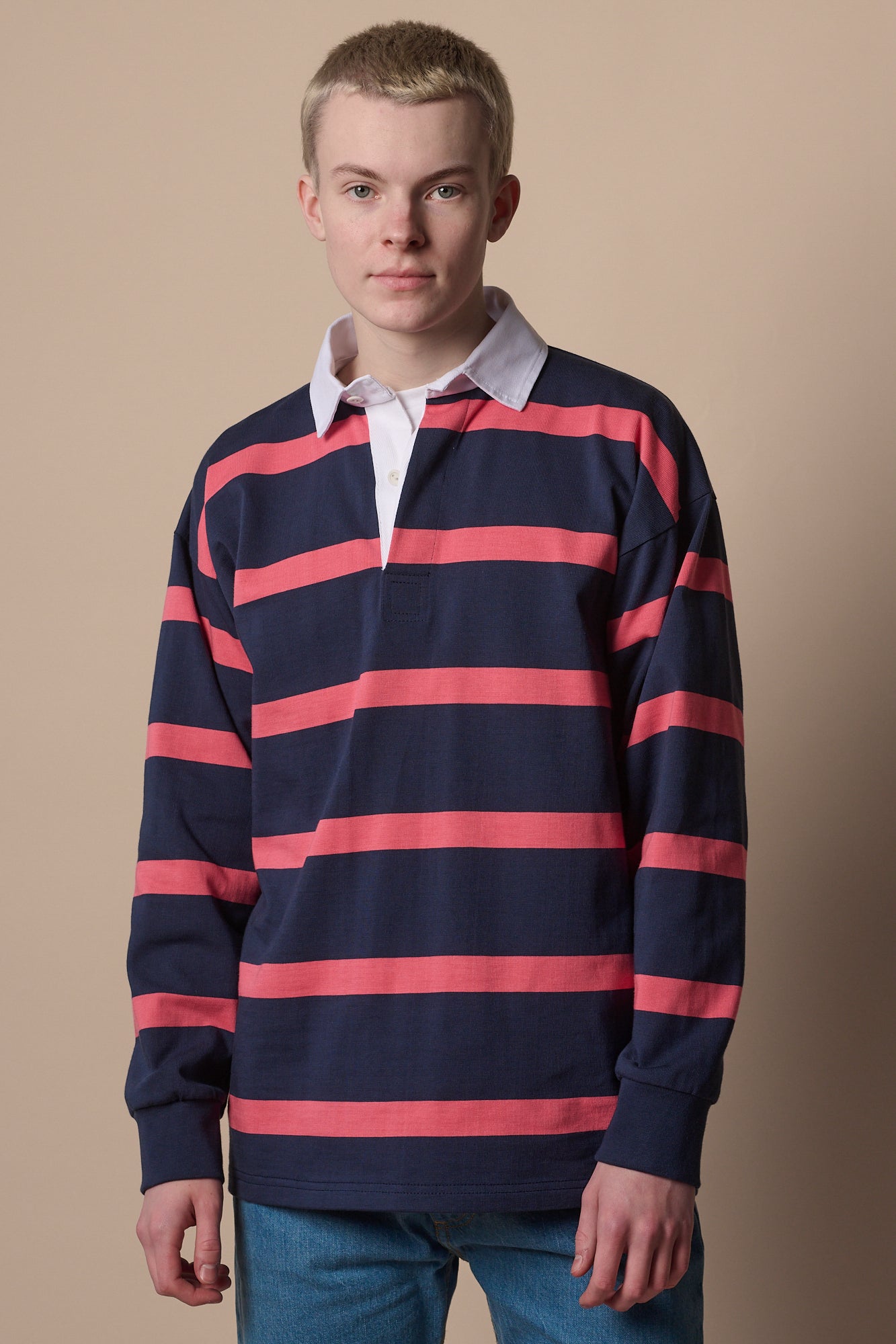 Thigh up image of white female wearing unisex striped rugby shirt in navy pink  tucked into jeans 