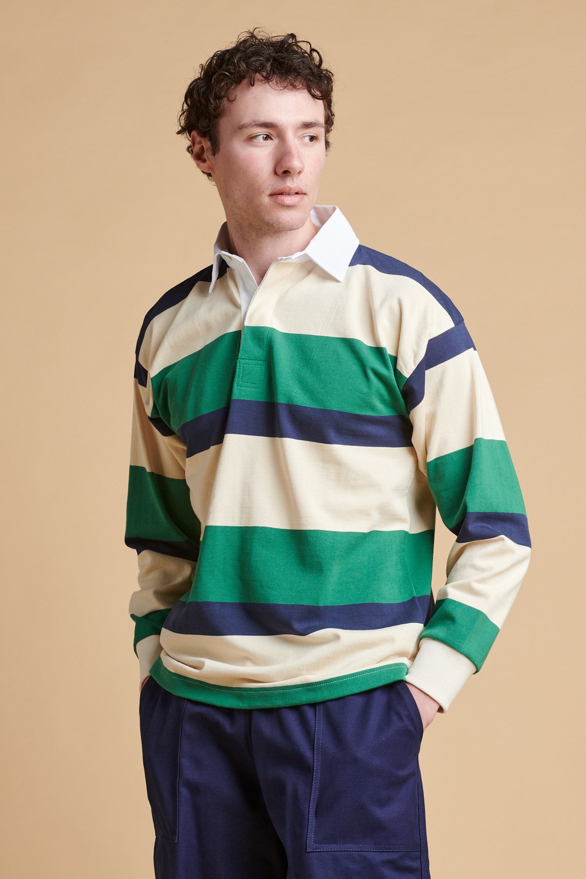 Male wearing striped rugby shirt in ecru navy bottle green paired with navy cameraman pants. 