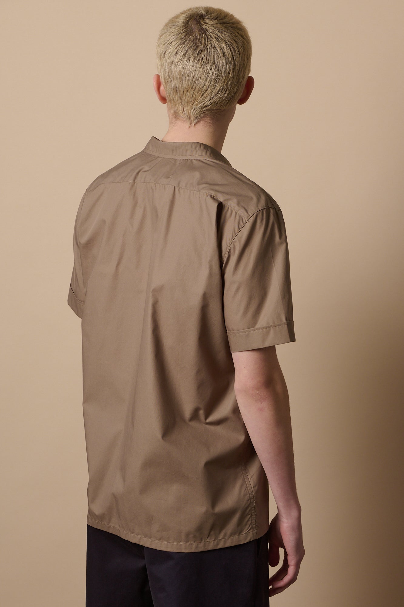 Thigh up image of the back of male with short blond hair wearing Tom short sleeve military shirt in khaki 
