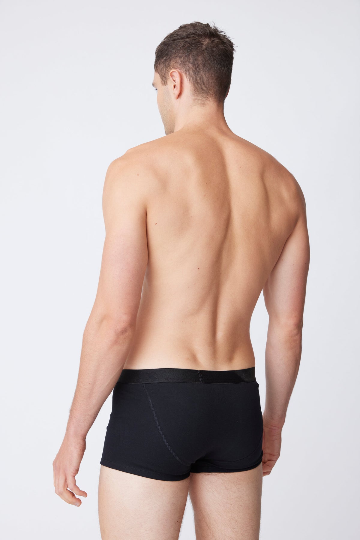 White male facing away wearing black trunks 