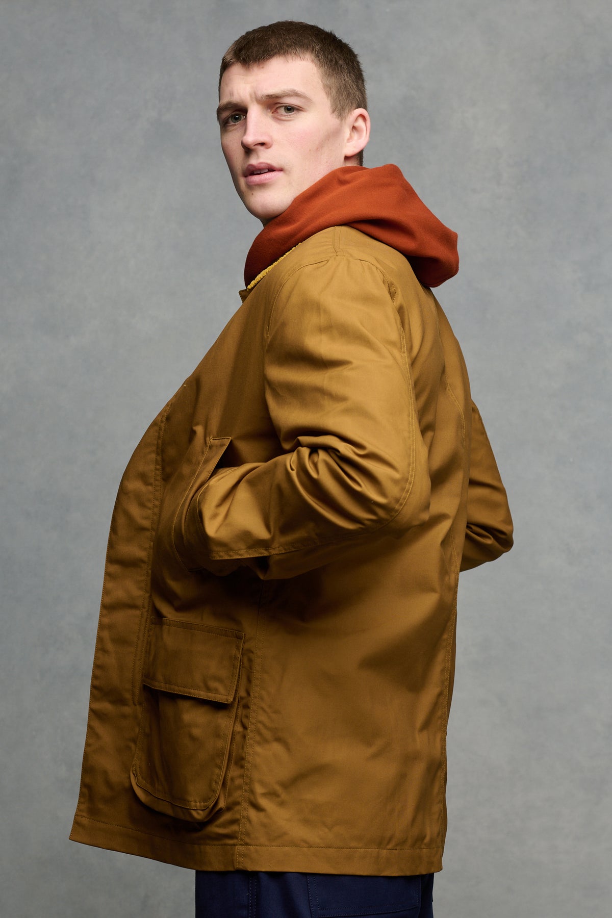 The side of brunet male wearing barn jacket in dark tan with hand in front pockets. 