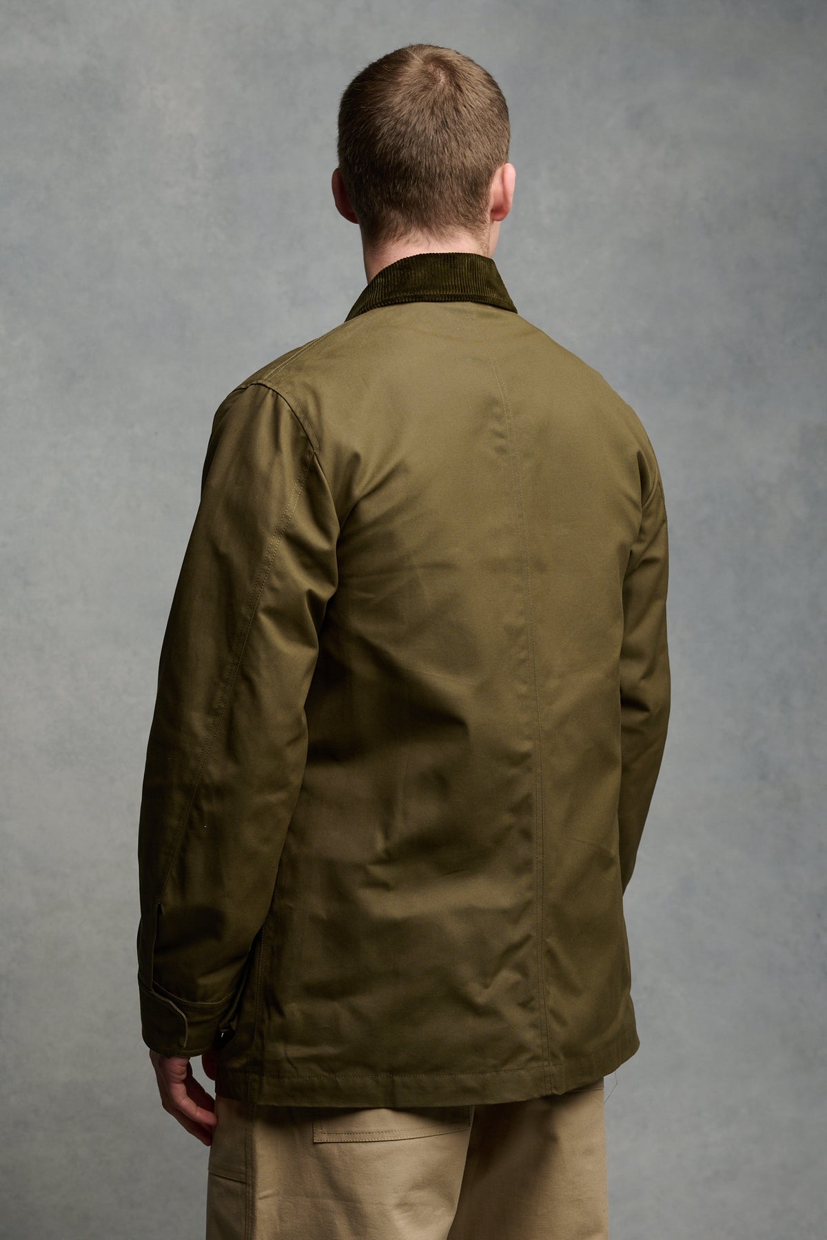 Thigh up image of brunet male from the back wearing barn jacket in olive with cord collar.