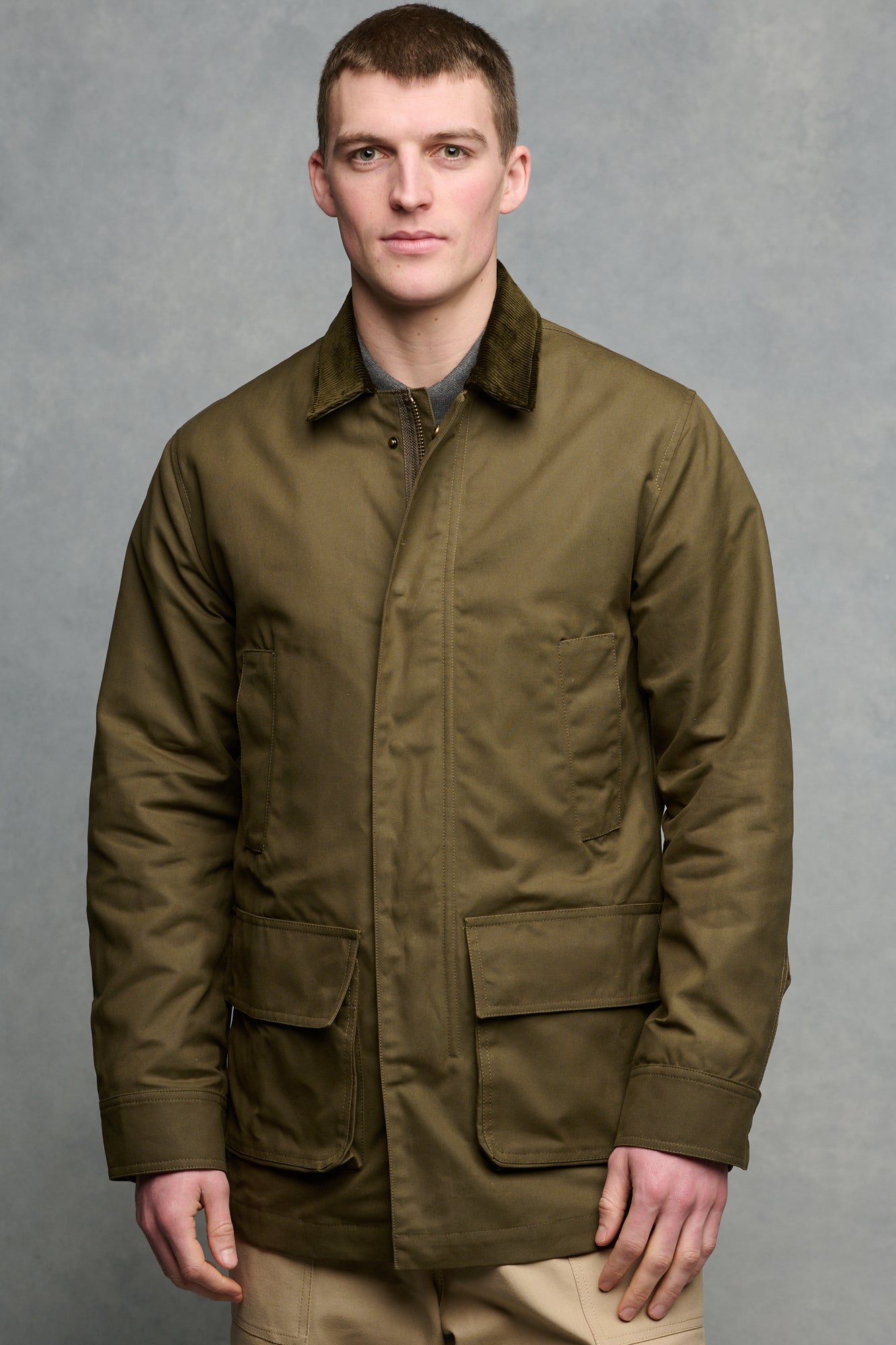 Thigh up image of brunet male wearing zipped and buttoned barn jacket with four front pockets.