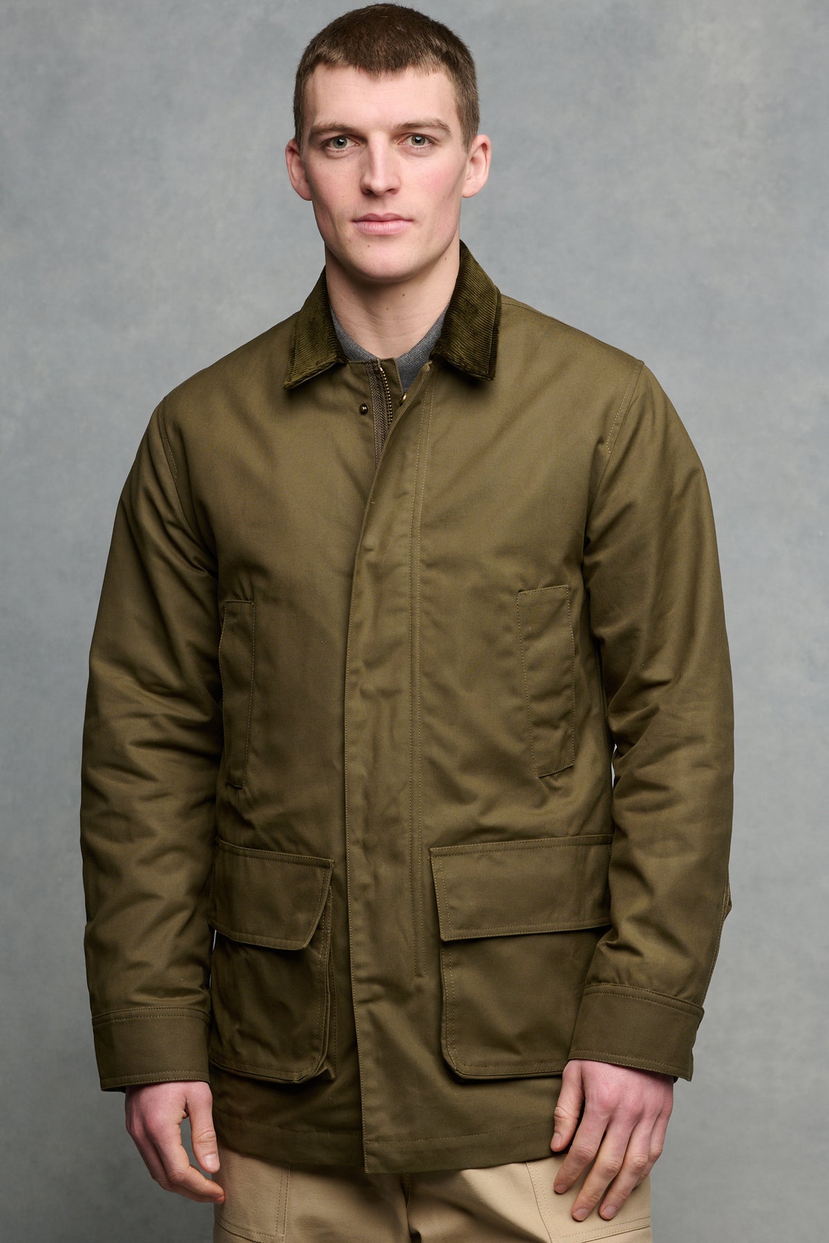 Thigh up image of brunet male wearing zipped and buttoned barn jacket with four front pockets.