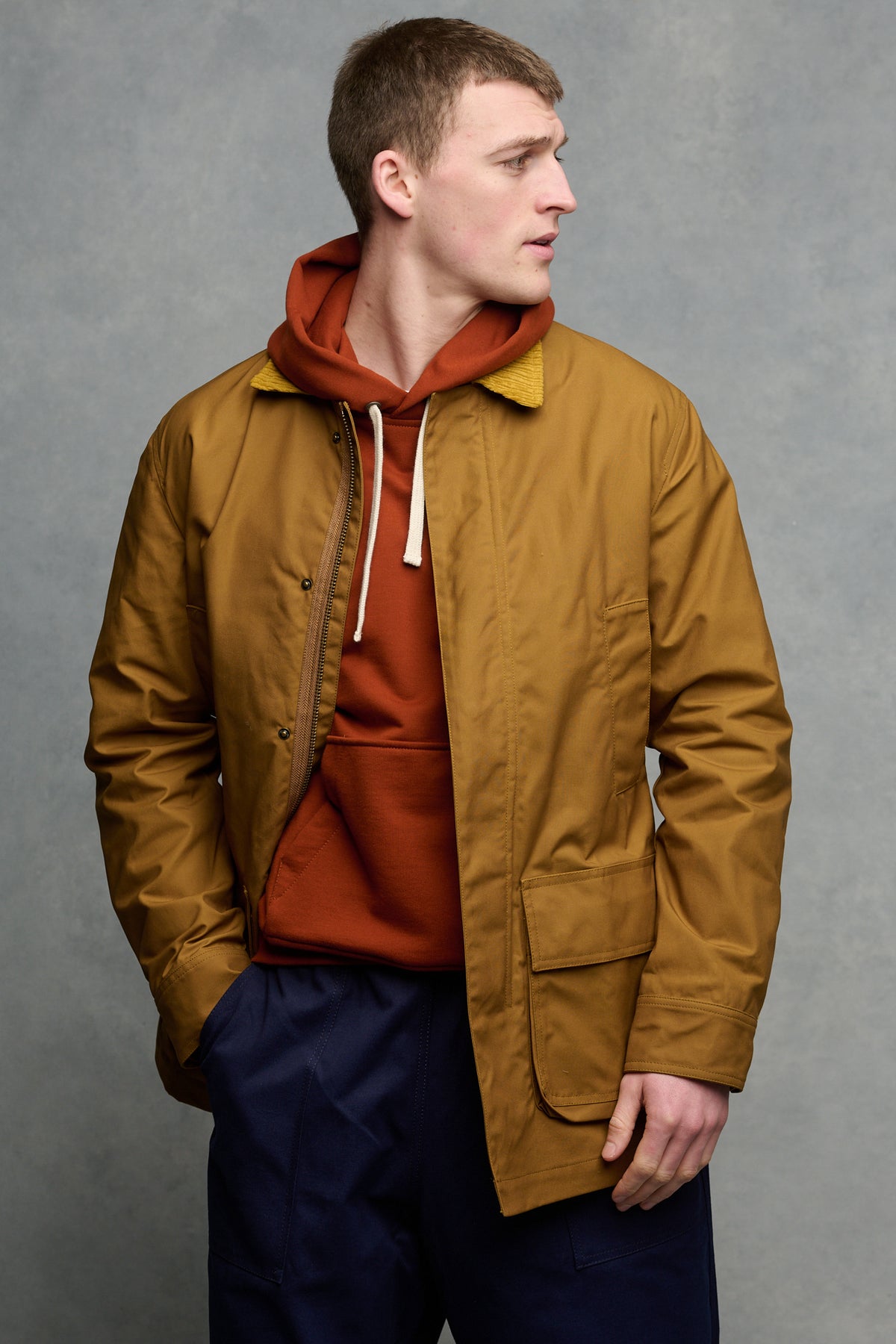 Thigh up image of male wearing barn jacket in dark tan unzipped over hooded sweatshirt in cinnamon