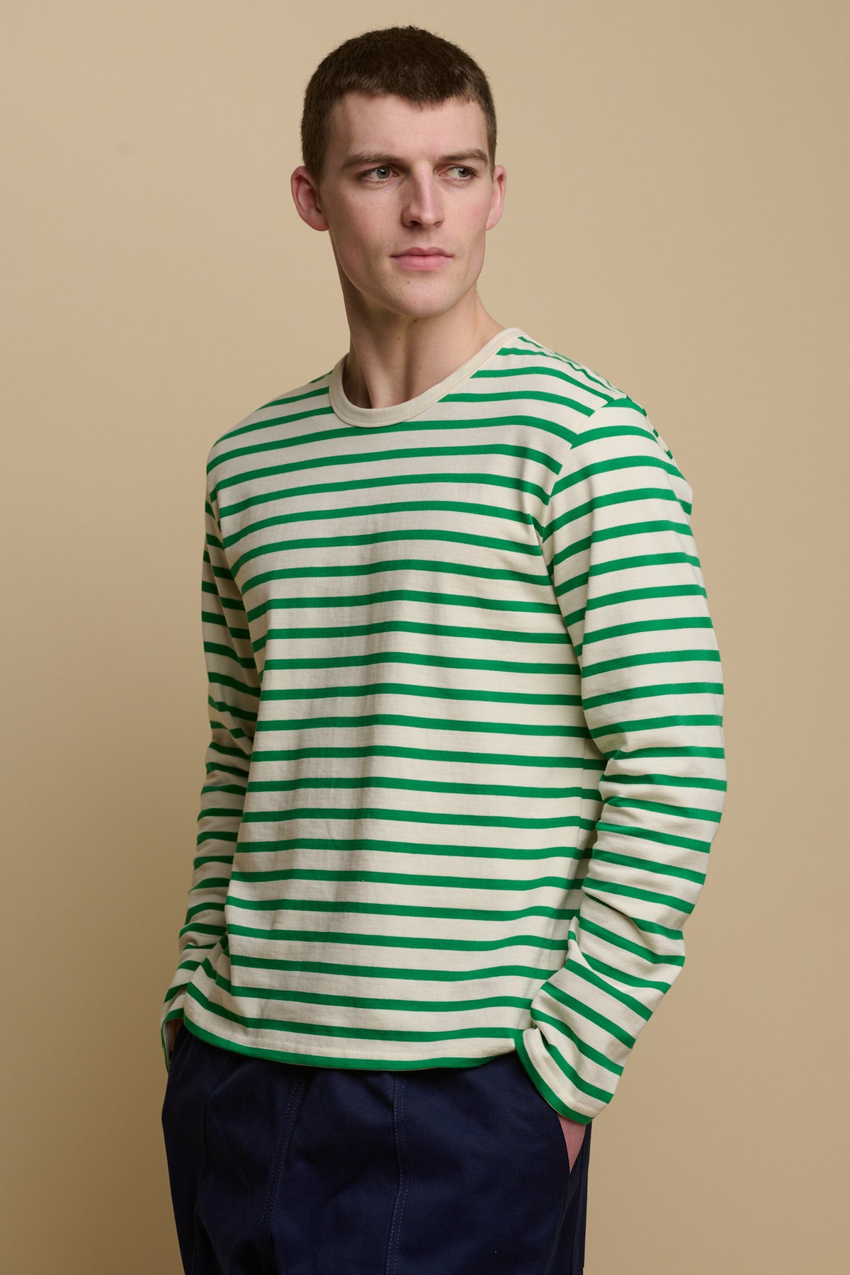 Thigh up image of male wearing Breton in ecru green with hands in pocket in cameraman pants in navy