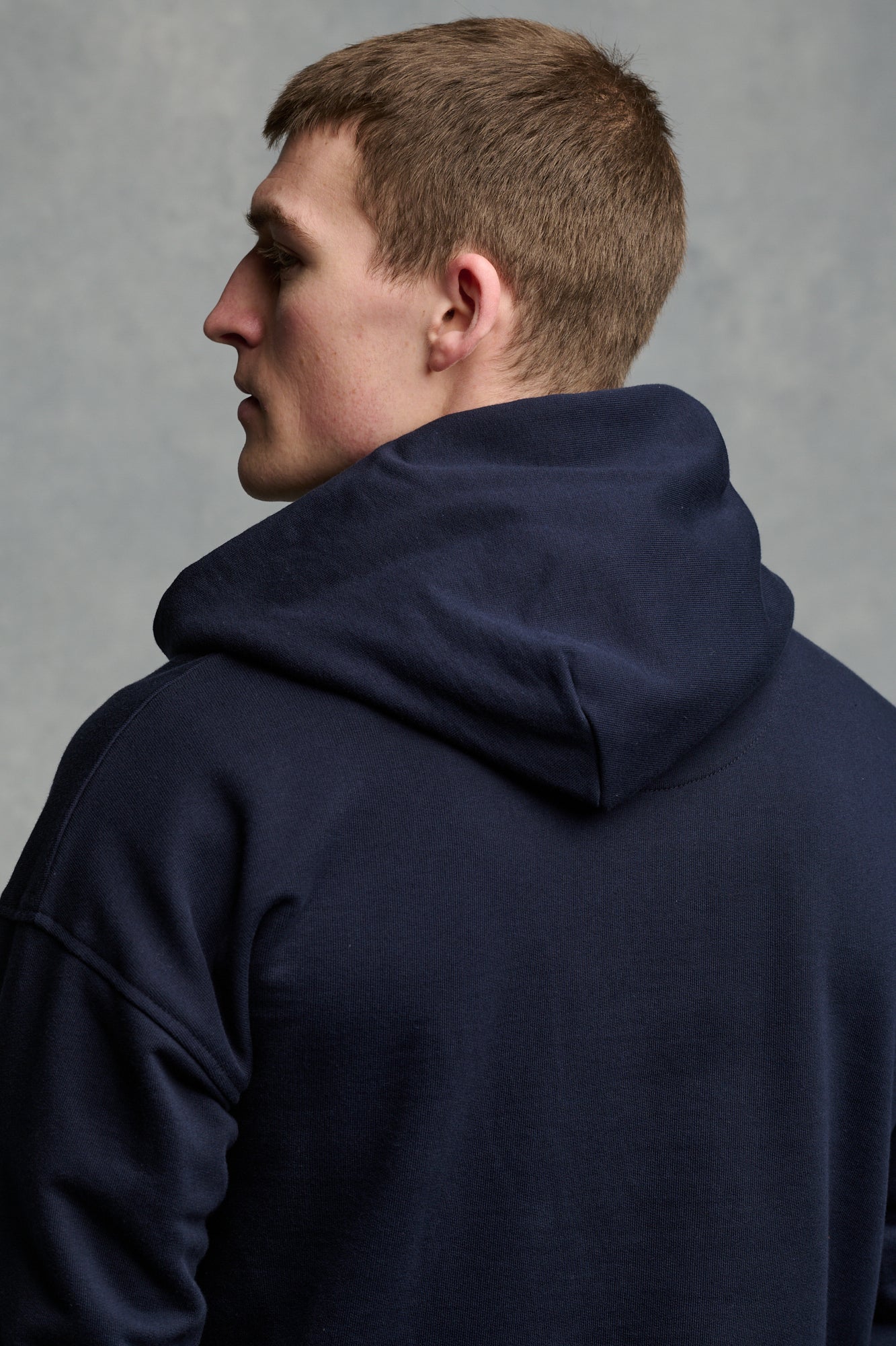 Thigh up image of male wearing hooded sweatshirt in navy with ecru drawstring through the hood
