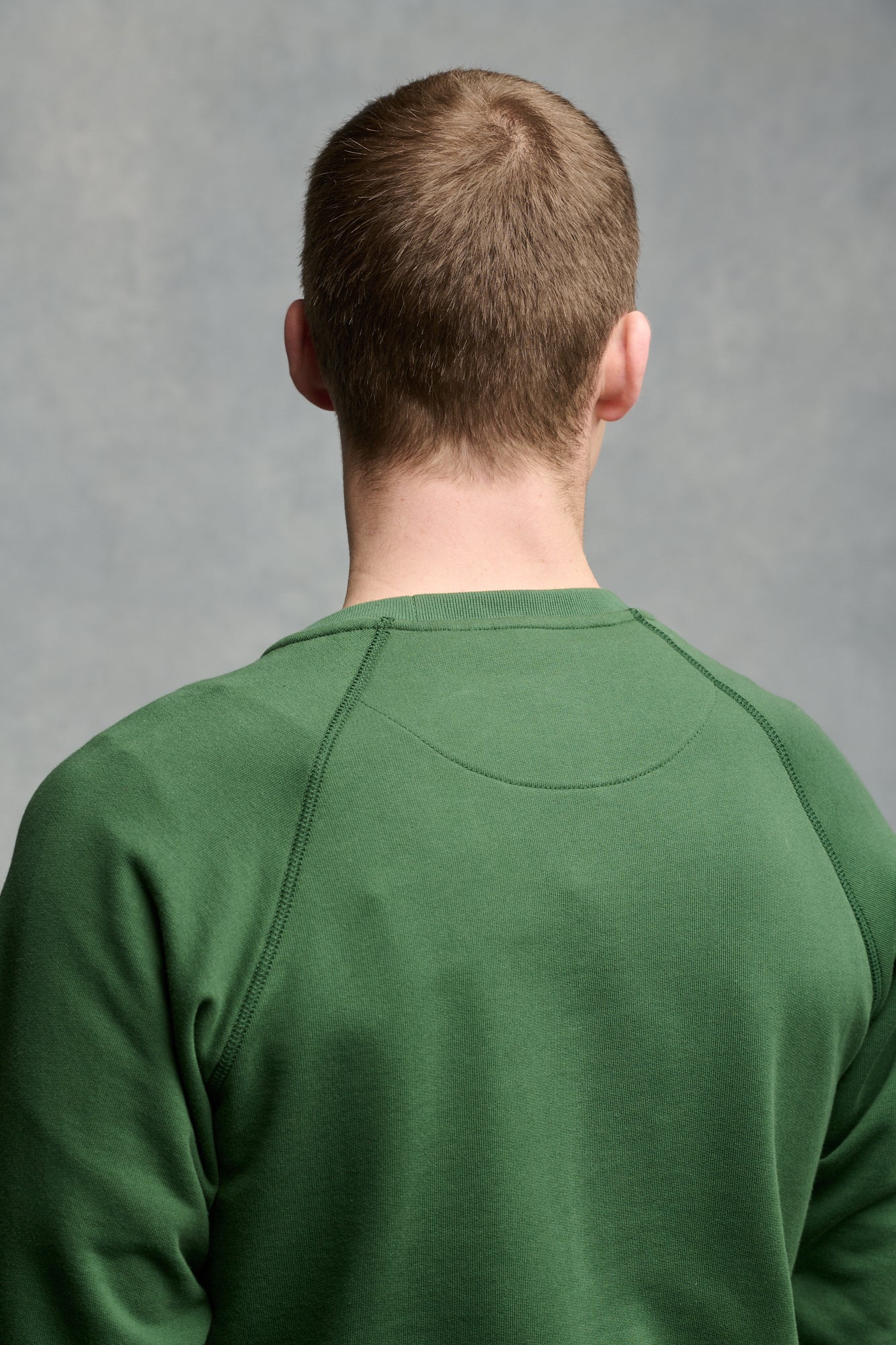 The back of male's shoulders wearing raglan sweatshirt in bottle green