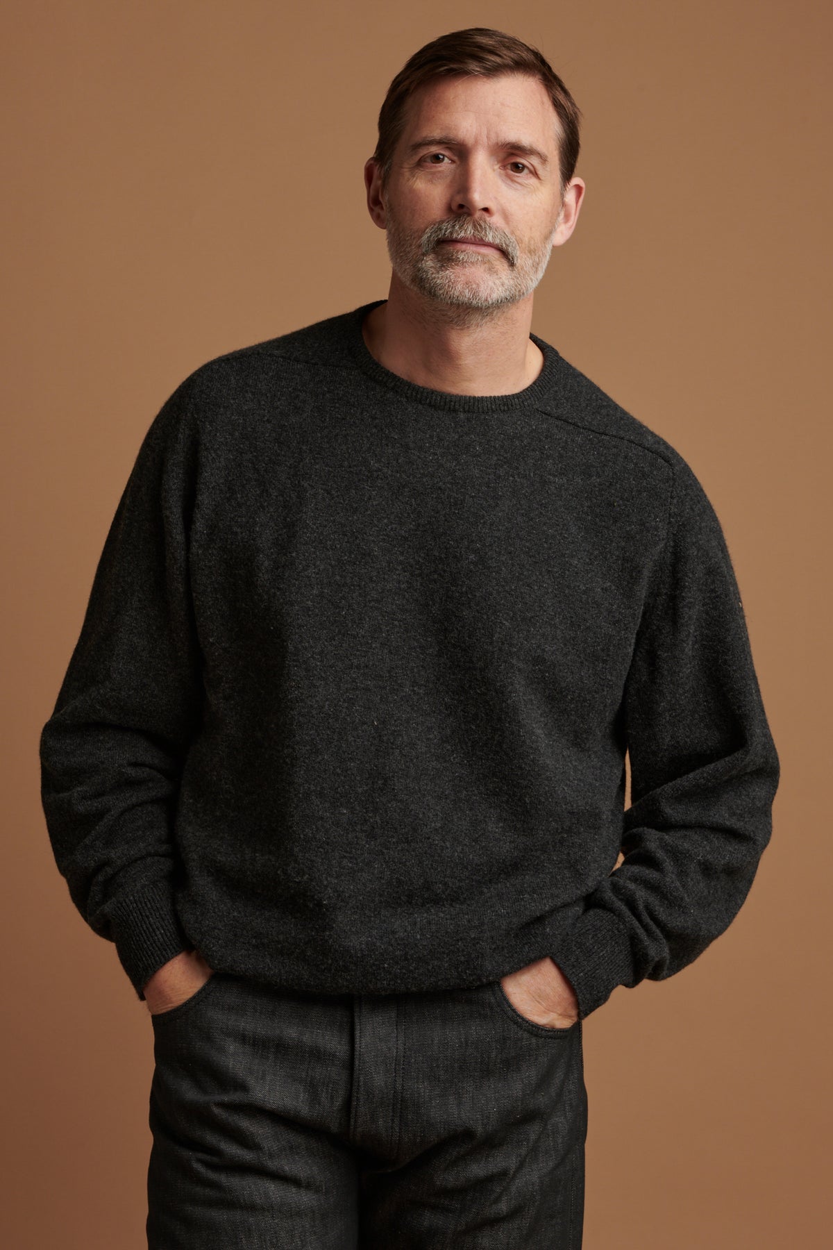 Patrick wearing lambswool saddle shoulder crew neck jumper in charcoal paired with loose fit button fly Arran jean in black