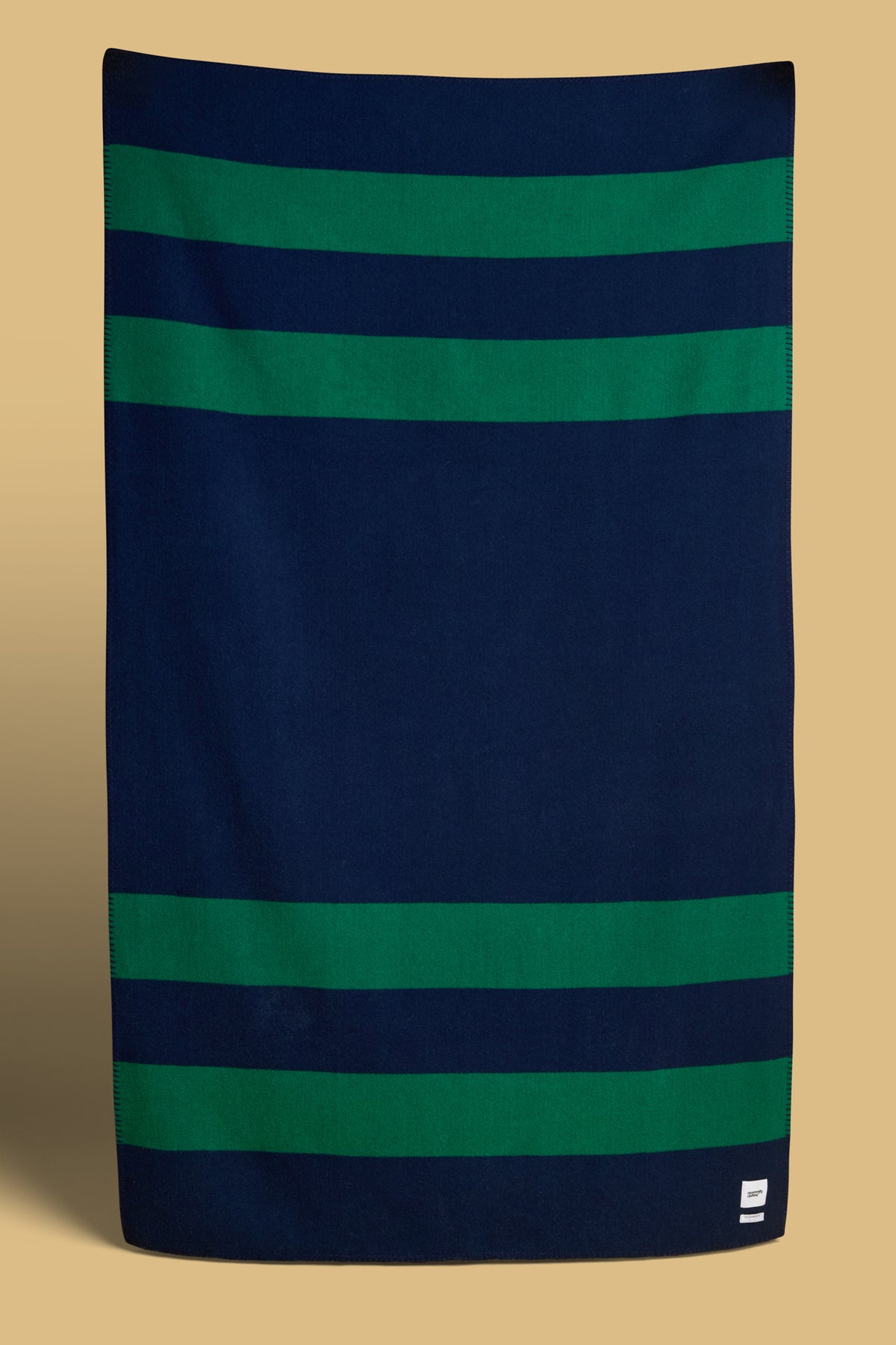 Blanket in navy and bottle stripe with woven Community Clothing logo in the bottom right hand corner.