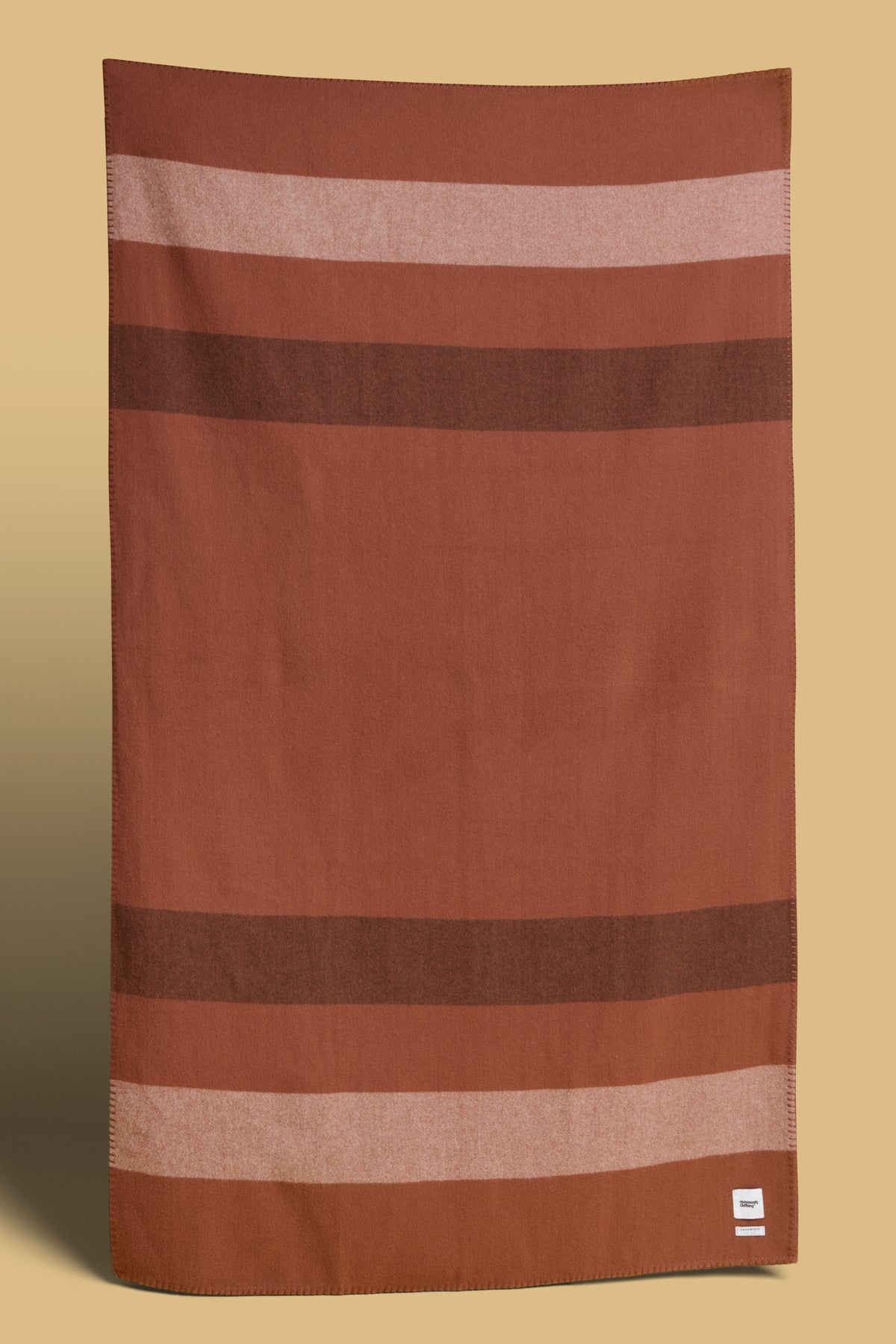 Blanket in tan with dark brown and ecru stripes, Community Clothing logo in bottom right hand corner of the blanket.