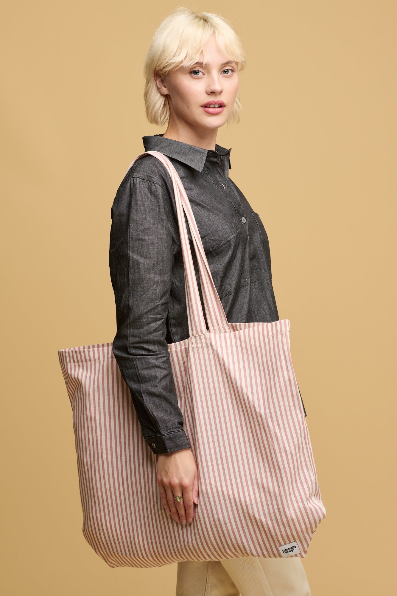 Female wearing quarry bank mill stripe tote bag in red and white stripe with small Community Clothing logo in the bottom right corner of the bag