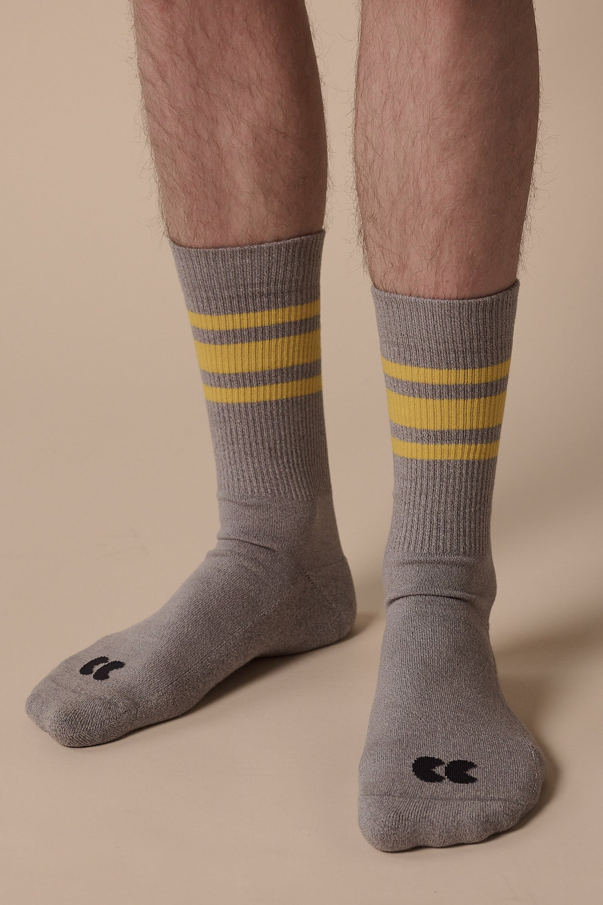 Image of below the knee of model wearing sports cotton sock calf length in grey with yellow stripes, and CC logo in black on the toe