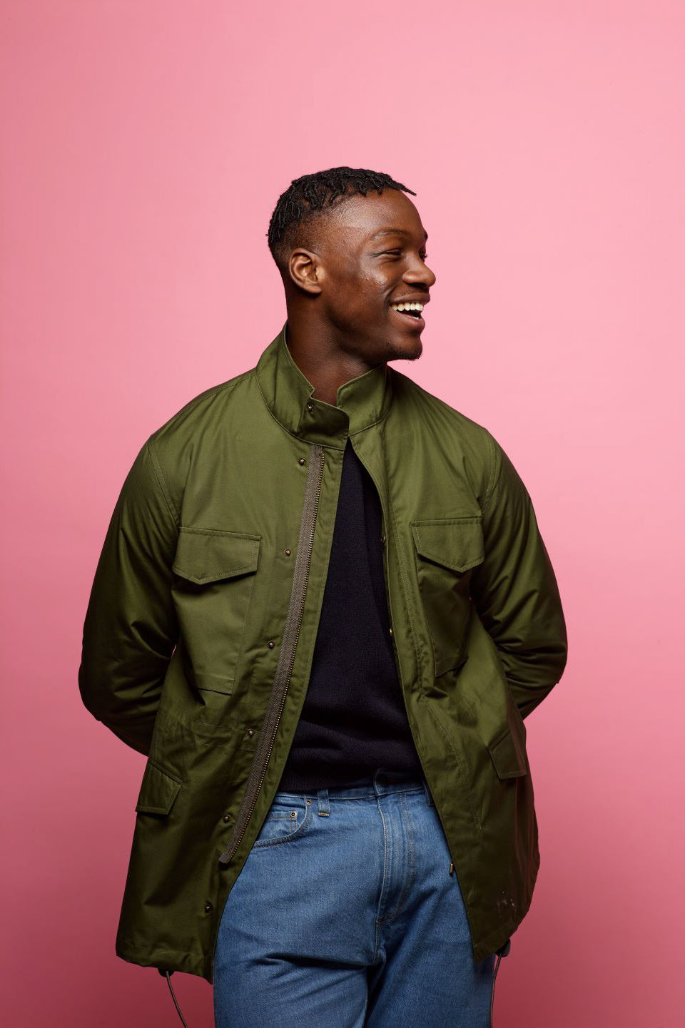 young black male smiling as he is wearing an olive field jacket from community clothing